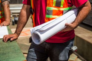 A construction worker with rolled up plans under his arms